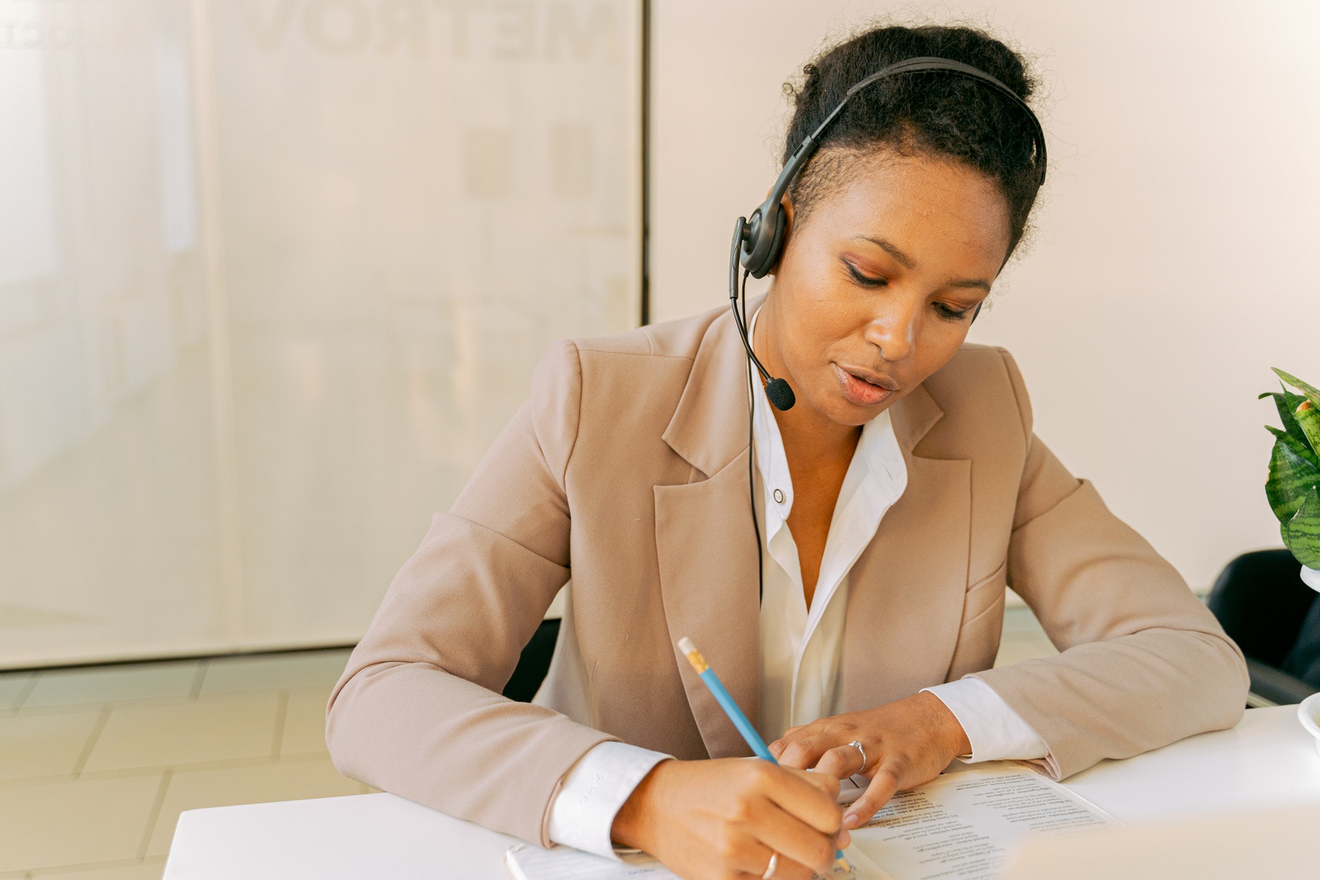 professionally dressed black woman takes notes while wearing a headset