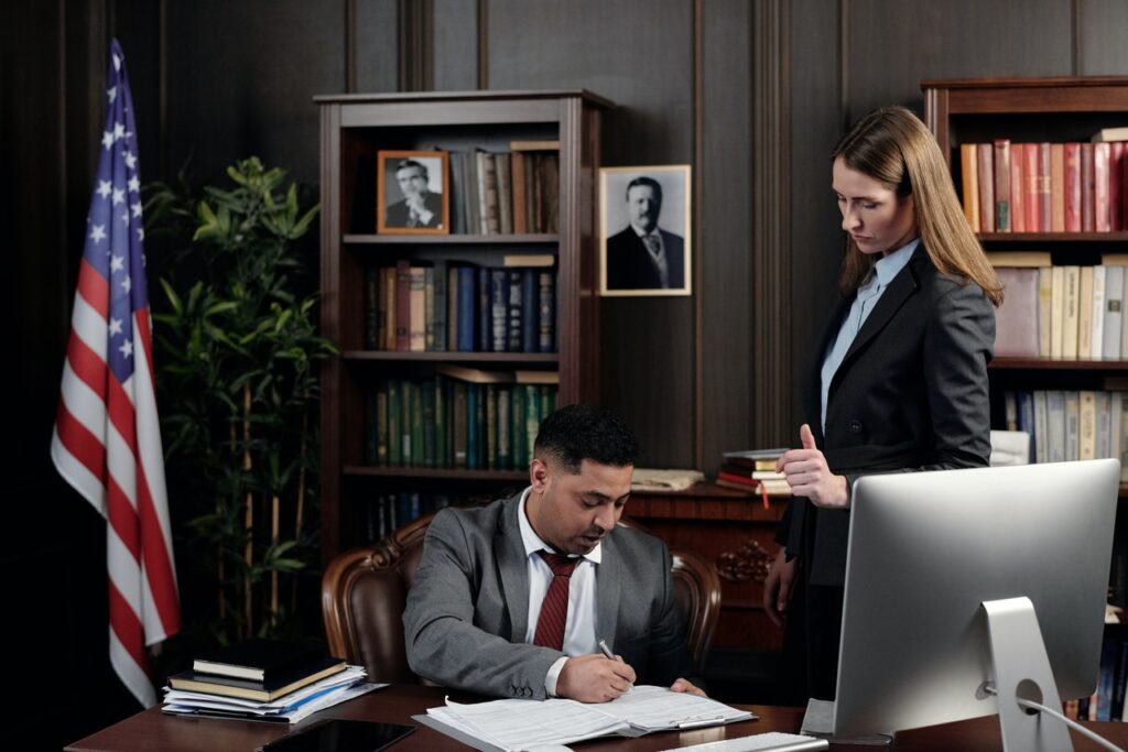 attorney works at desk while paralegal stands nearby