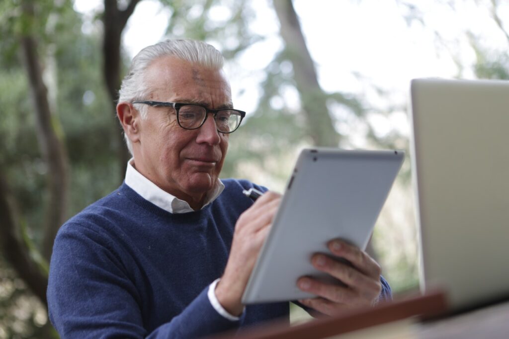 silver haired man works on an ipad with nature background