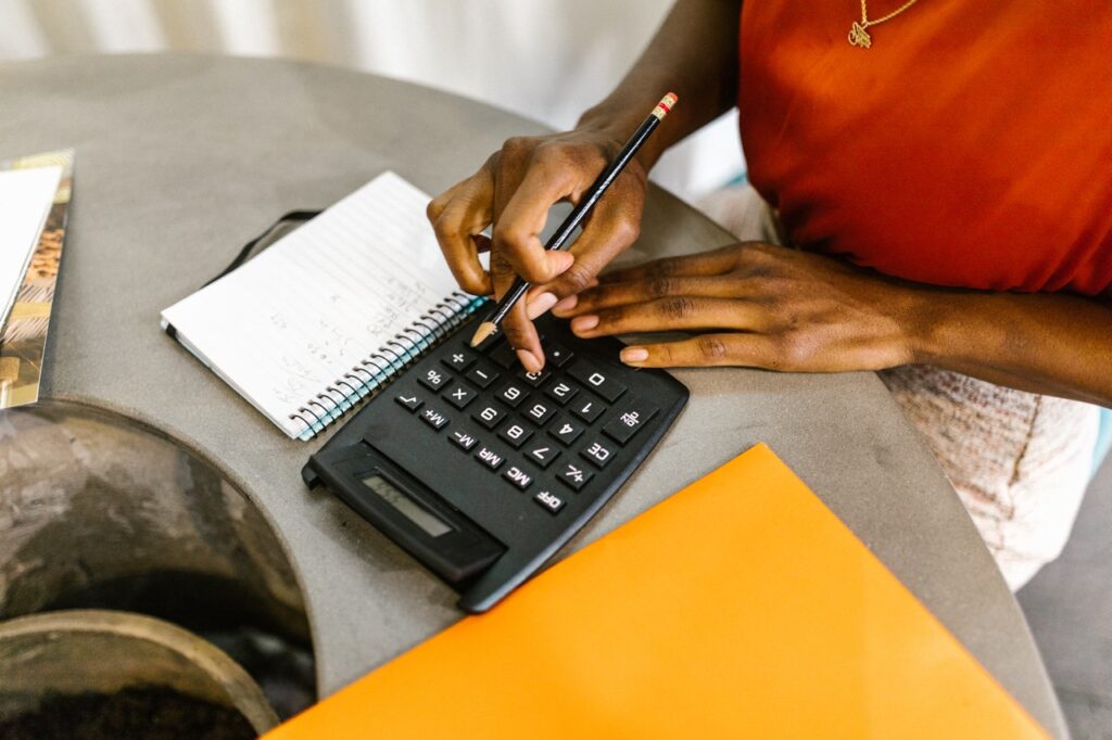 black woman types on calculator with notepad and manila envelope