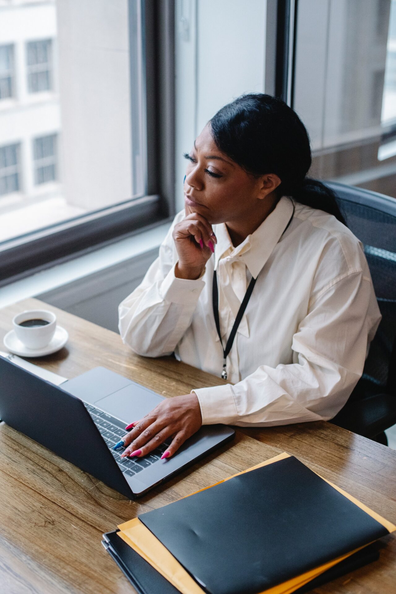 black woman sits at computer desk looking at laptop contemplatively