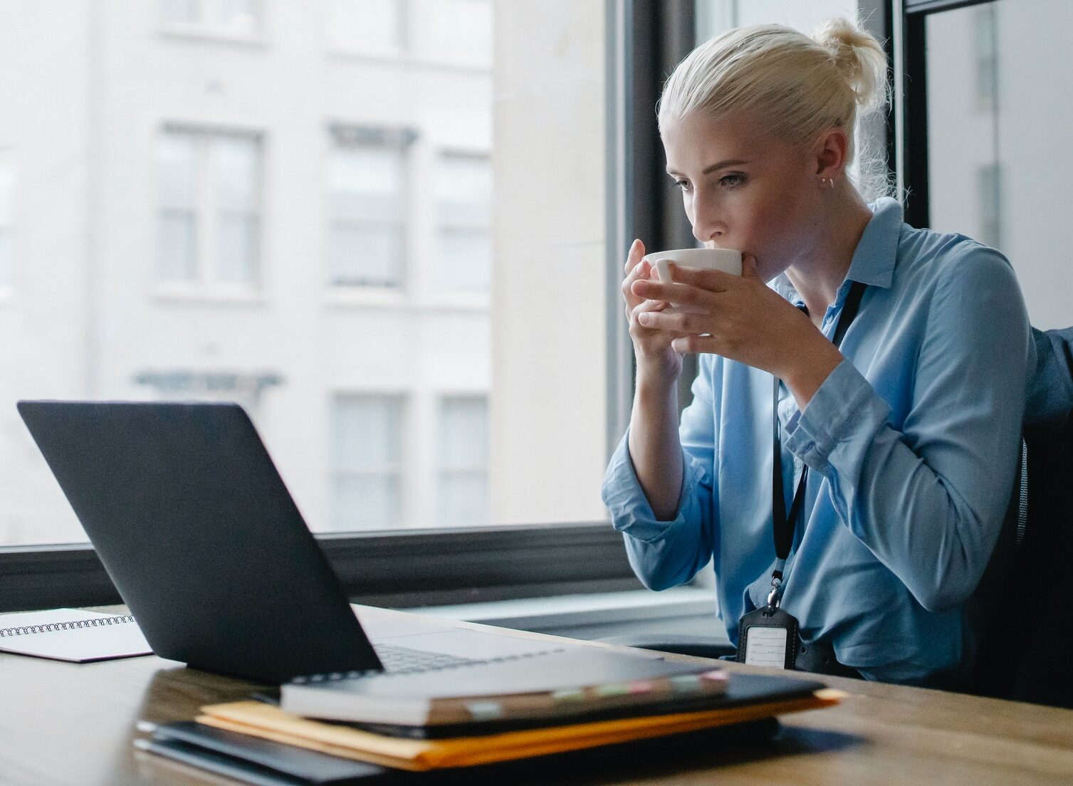 professional woman seated at desk sipping coffee while looking at laptop