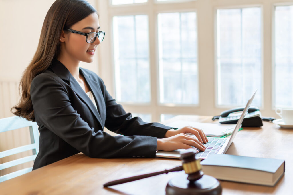 young female lawyer types on laptop while seated at desk in law office